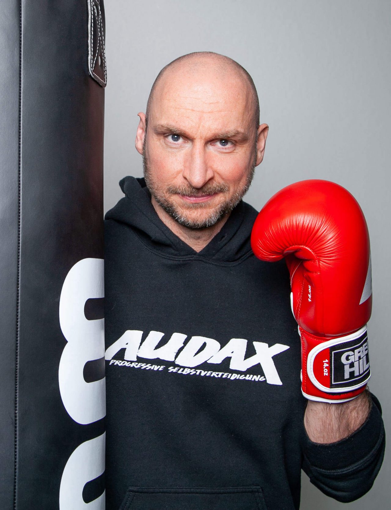 Kampfsport und Selbstverteidigungstrainer Christian steht mit einem Boxhandschuh am Sandsack